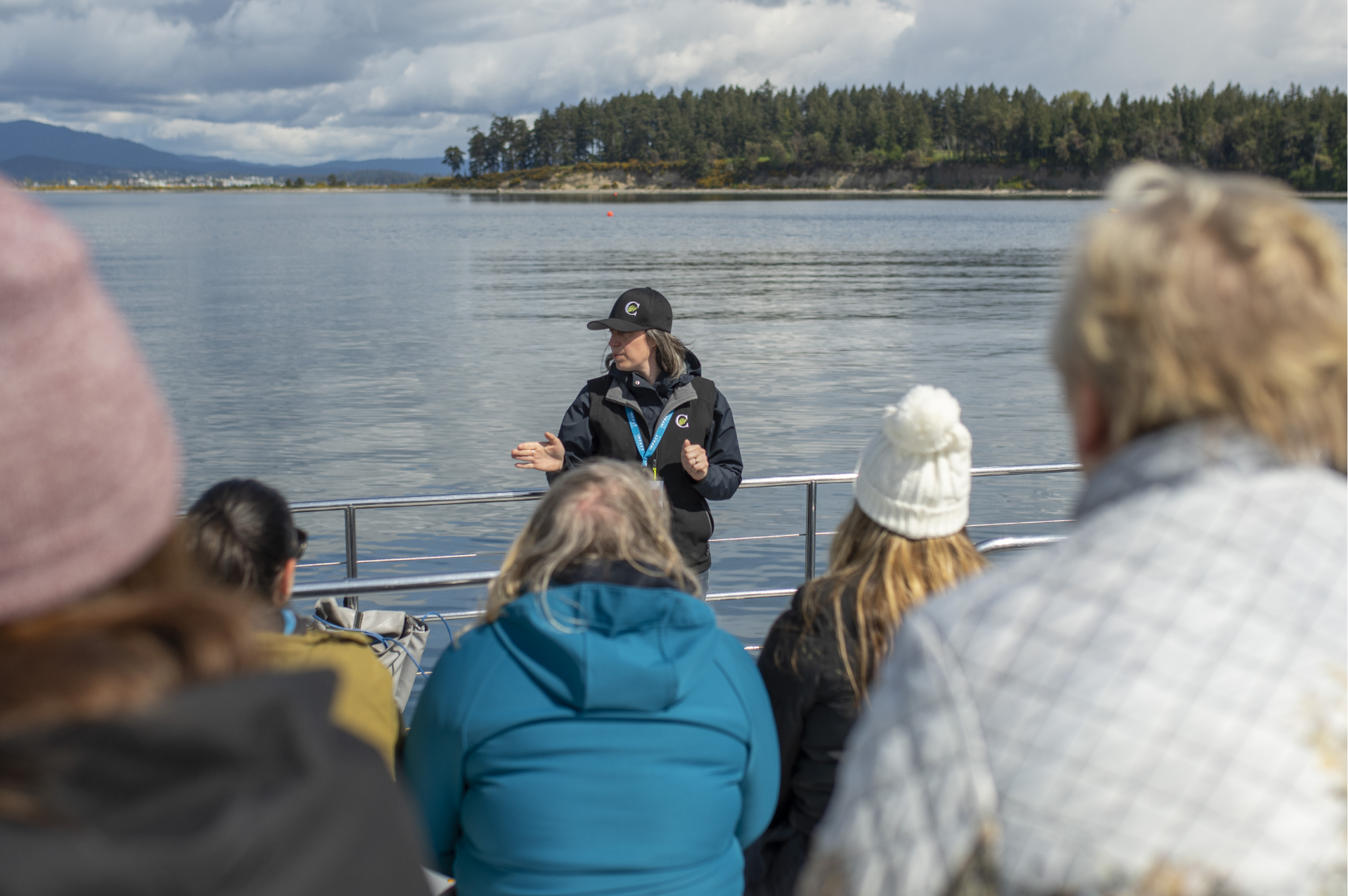 Woman speaking at a conference outdoors with the ocean and trees in the background.